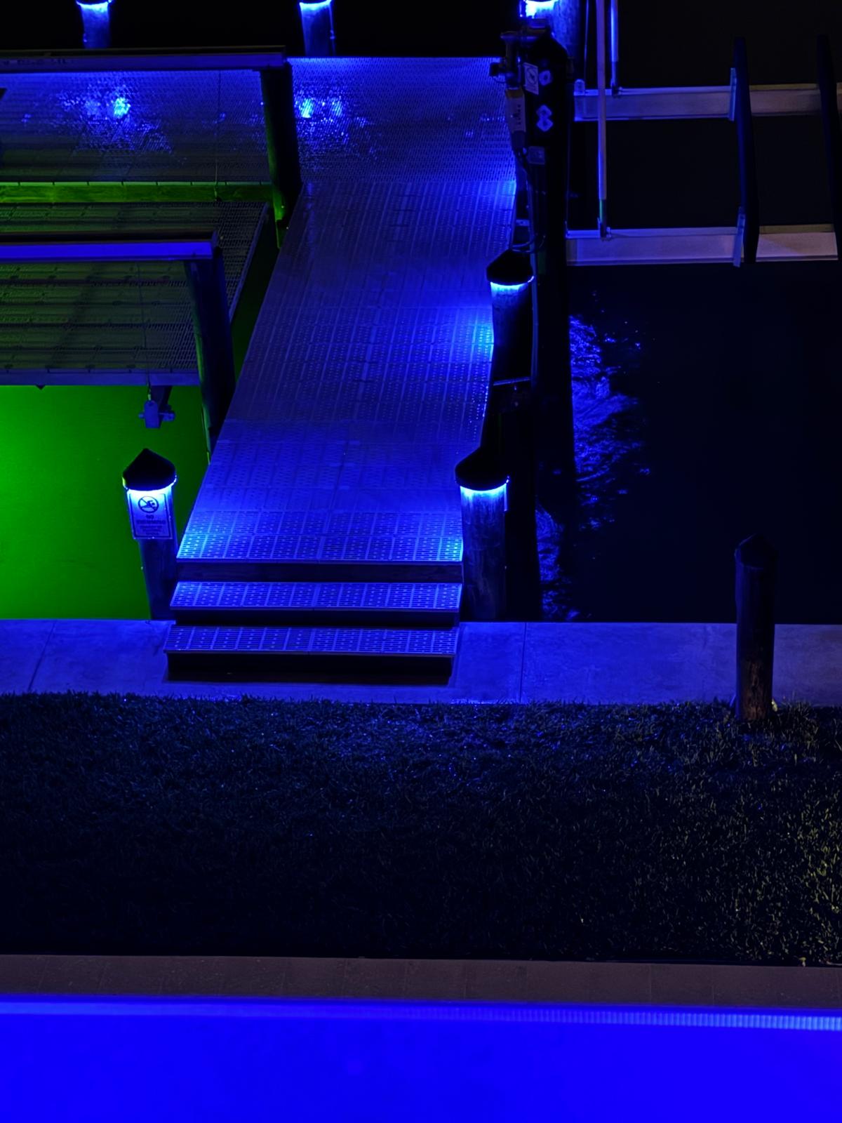 Dock illuminated with green and blue piling cap lights at night over a body of water 