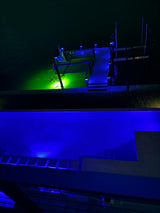 Dock illuminated with 
 blue piling cap lights at night over a body of water with city skyline
