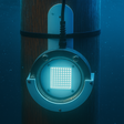 DV59 Underwater light fixture with bracket on a wooden post with a blue glow against a dark blue underwater background.